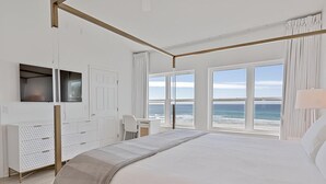 A bedroom with a large bed, a desk, a TV, and a view of the ocean. - Gulfs Edge Townhome #7- Sun-kissed Memories (Panama City Beach)