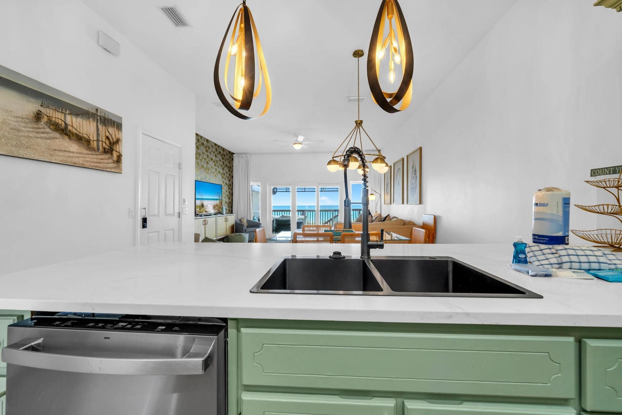 Una cocina moderna con lavavajillas de acero inoxidable, una isla grande con pileta e iluminación colgante.