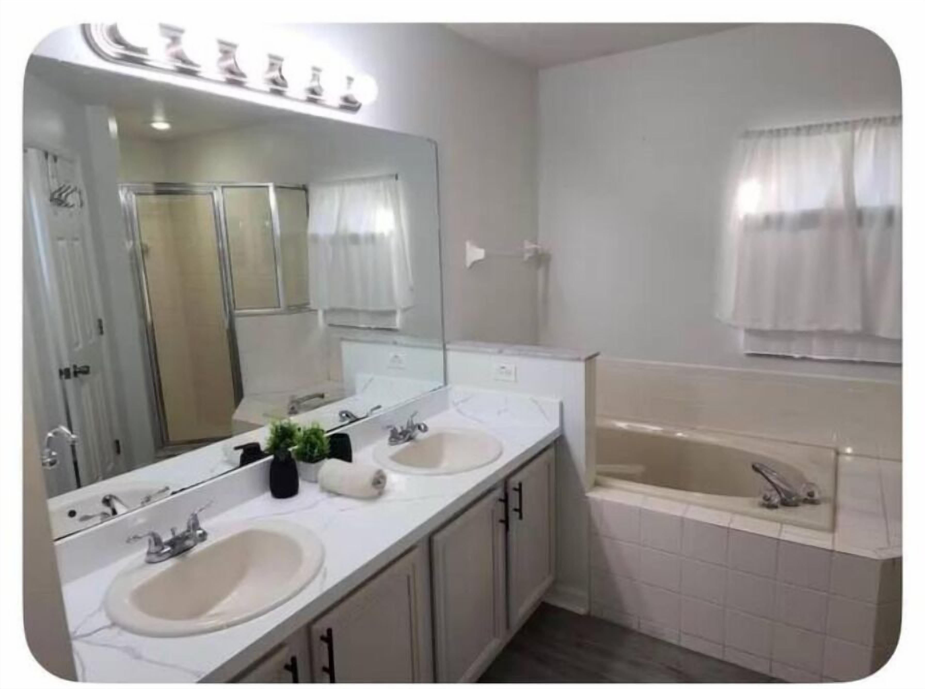 Un baño con dos lavamanos, un espejo grande y una bañera.