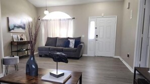 Ein Wohnzimmer mit grauem Sofa, einem Couchtisch mit Vase und Skulptur, und einer Tür im Hintergrund.