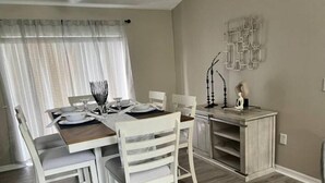 Ein Essbereich mit einem Tisch für vier Personen, weißen Stühlen, einer Schrank mit Regalen und einer Wanddekoration.