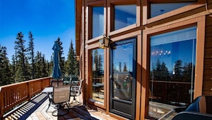 Eine Holzterrasse mit Gartenmöbeln, einer Glastür und Blick auf einen Wald.