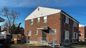 A two-story brick building with a flat roof, a small porch, and a visible garage door. - 3-bedroom townhome Summer Rental in fabulous Hyattsville with WiFi, AC (Hyattsville)