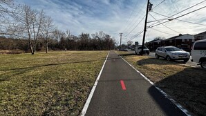 A paved path with a red line, flanked by grass and trees, leading to a residential area with houses and parked cars. - 3-bedroom townhome Summer Rental in fabulous Hyattsville with WiFi, AC (Hyattsville)
