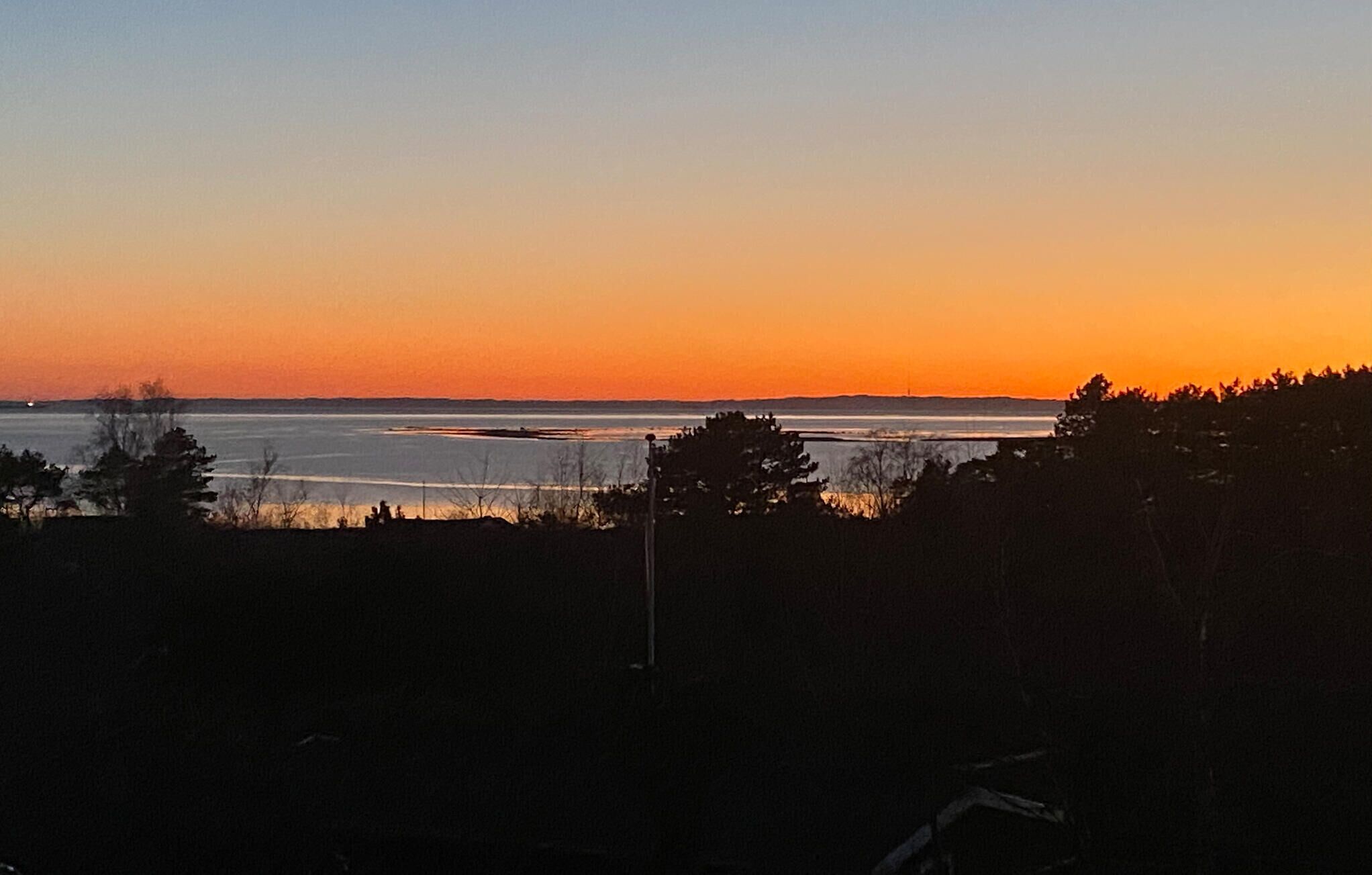 Un paysage côtier au coucher du soleil, avec une vue sur la mer et la terre au loin.