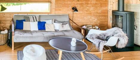 A cozy cabin interior with a grey sofa, a rocking chair, a small table, and a fireplace.