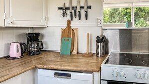 A kitchen with a white dishwasher, a coffee maker, a cutting board, a knife rack, and a stove.