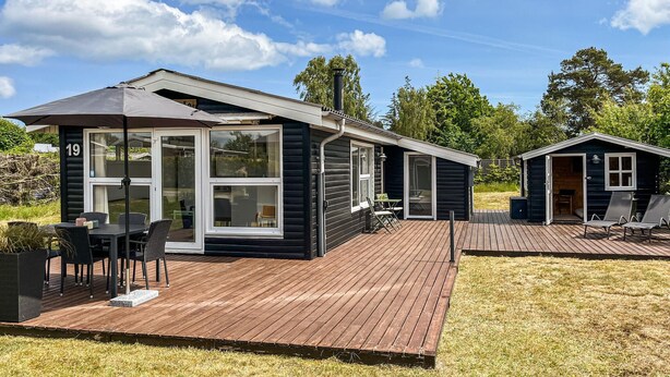 A modern log cabin with a deck, outdoor seating, and a large window.