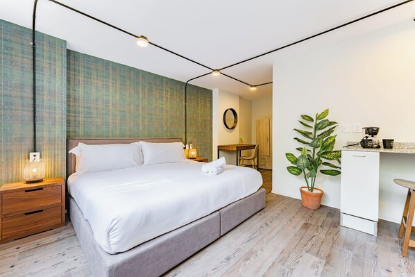 Ein modernes Schlafzimmer mit einem großen Bett, Nachttischen, einem kleinen Schreibtisch und einer Topfpflanze.