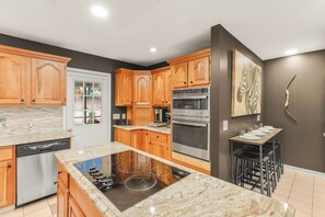 A modern kitchen with wooden cabinets, a built-in oven, a dishwasher, and a dining area with a table and chairs.
