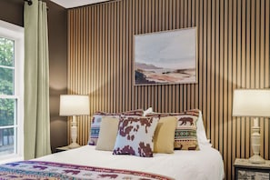 A hotel room with a bed, pillows, a painting, and a window.