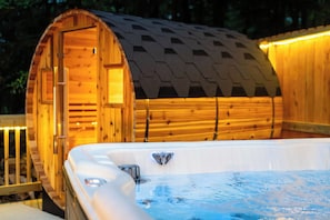 Una vasca idromassaggio in legno con cascata, circondata da un pontile in legno e un'area coperta con tetto spiovente.