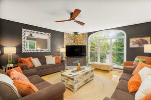 A modern living room with a large flat-screen TV, a ceiling fan, and a stone accent wall.