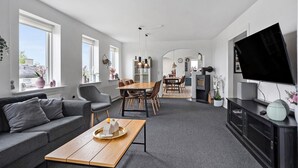 A modern living room with a sofa, coffee table, TV, and a dining area with chairs and a table. - 6 bedroom amazing home in Glesborg (Glesborg)