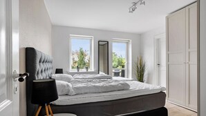 A modern bedroom with a large bed, two windows, a door, and a small table. - 6 bedroom amazing home in Glesborg (Glesborg)