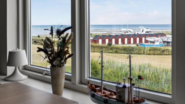 A room with a large window overlooking a beach with boats and red buildings. - 6 bedroom amazing home in Glesborg (Glesborg)