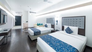 A hotel room with two beds, a desk, a chair, a TV, a ceiling fan, and a door leading to a bathroom. - Hotel Deccan Serai Grande (Hyderabad)