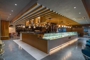 A modern cafe with a wooden counter, hanging lights, and a glass display case. - Hotel Deccan Serai Grande (Hyderabad)
