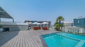 A rooftop pool area with a wooden deck, lounge chairs, and umbrellas. - Hotel Deccan Serai Grande (Hyderabad)