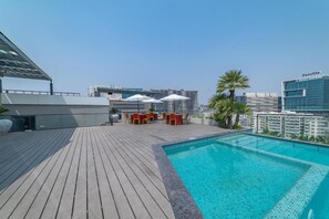 A rooftop pool area with a wooden deck, lounge chairs, and umbrellas. - Hotel Deccan Serai Grande (Hyderabad)