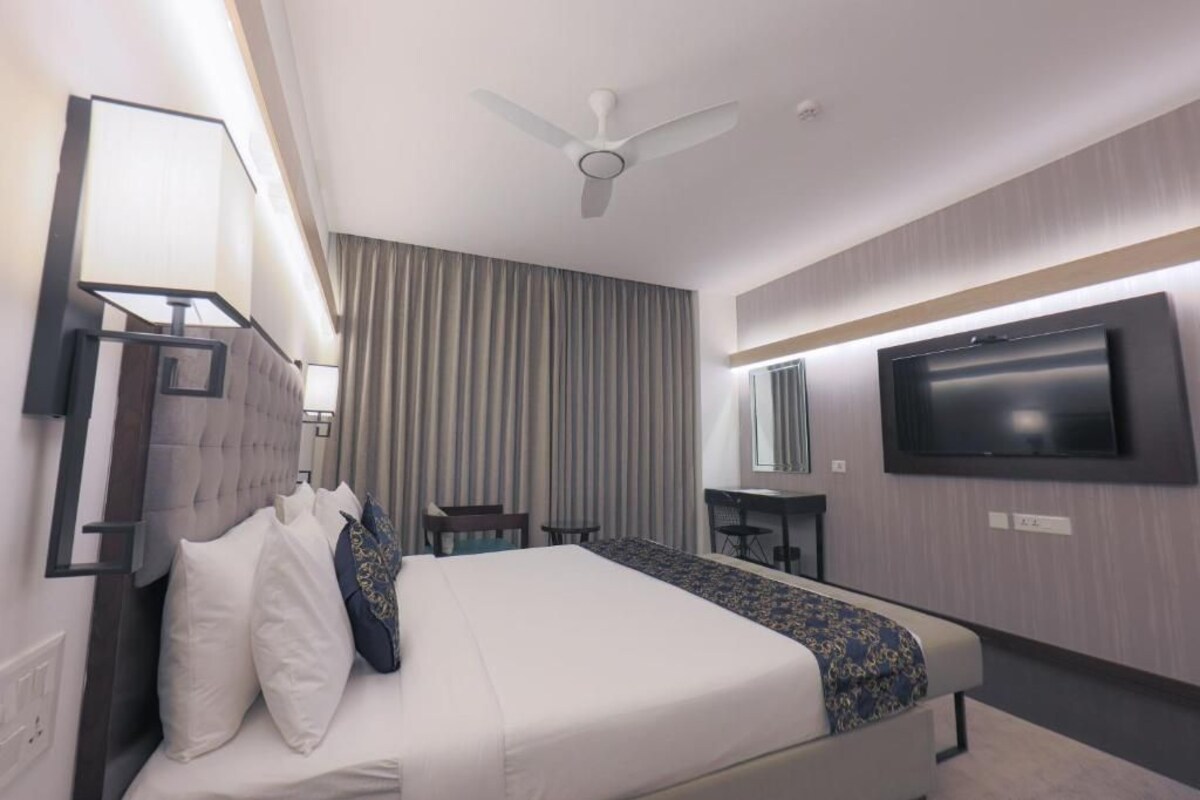 A hotel room with a bed, a desk, a chair, a TV, and a ceiling fan.