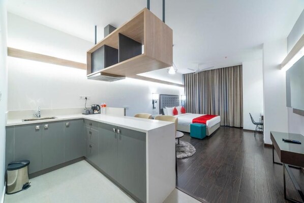 Een moderne hotelkamer met een kitchenette, een bed met rode beddengoed, een bureau en een stoel.