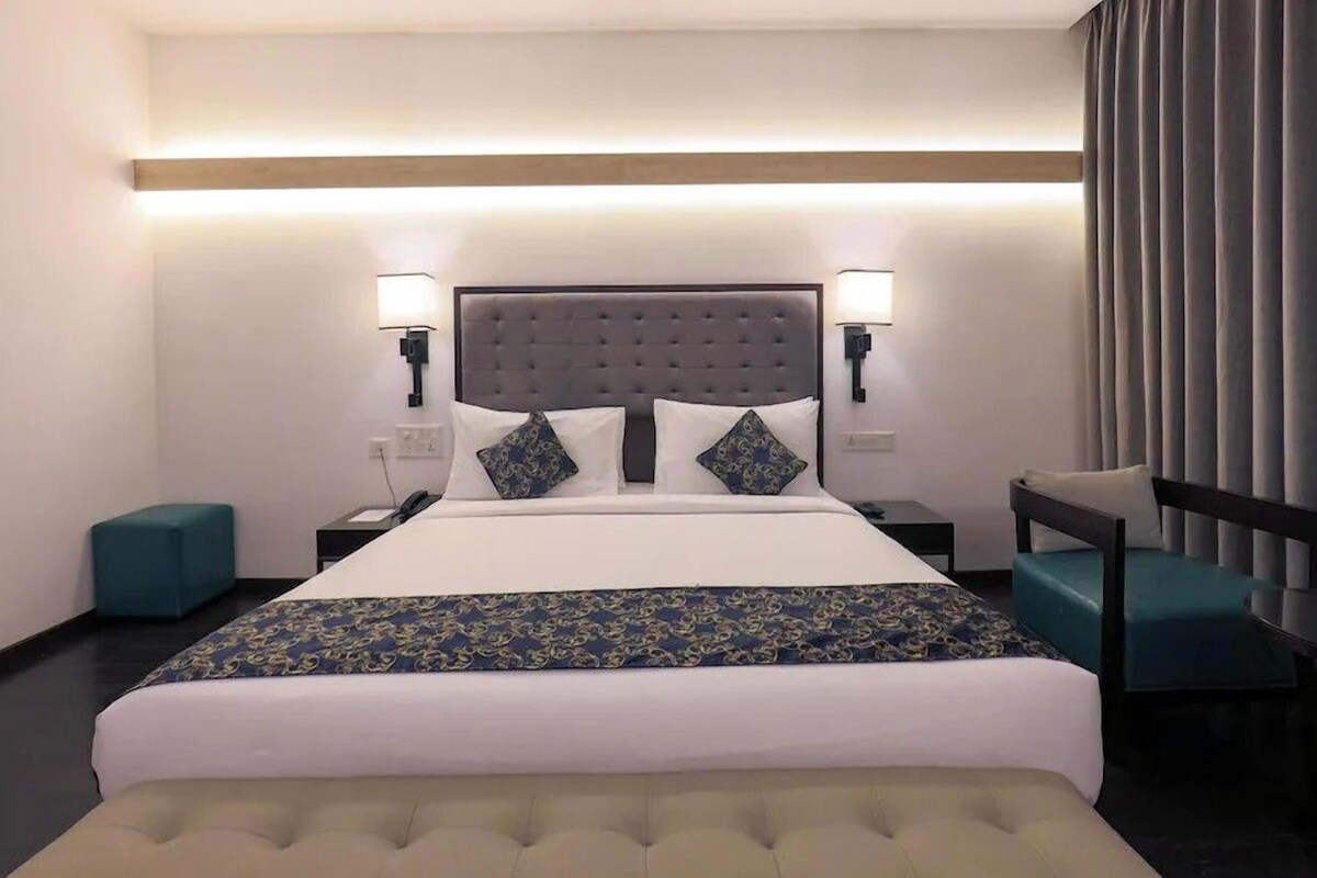 A hotel room with a large bed, two bedside tables, a chair, and a desk.