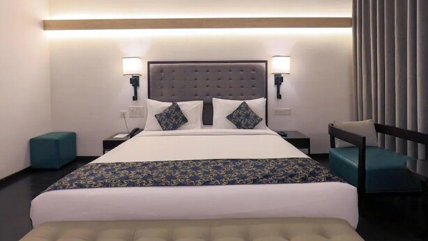 A hotel room with a large bed, two bedside tables, a chair, and a desk. - Hotel Deccan Serai Grande (Hyderabad)