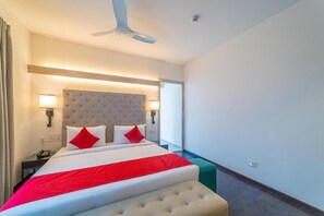 Een hotelkamer met een groot bed, een plafondventilator, een nachtkastje met telefoon en een raam met uitzicht.