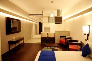 A hotel room with a bed, a desk, two chairs, a sofa, and a TV. - Hotel Deccan Serai Grande (Hyderabad)