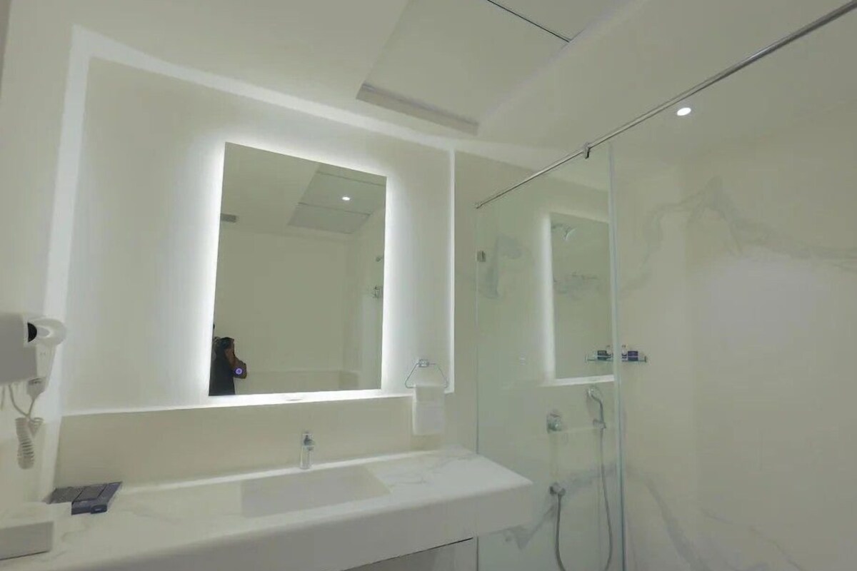 Een moderne badkamer met een grote spiegel, een wit wastafelmeubel en een douchecabine.