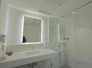 A modern bathroom with a large mirror, a white sink, and a glass-enclosed shower area. - Hotel Deccan Serai Grande (Hyderabad)