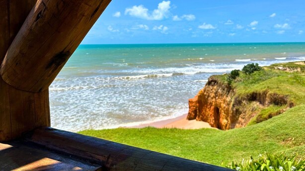 A wooden deck overlooking a beach with clear skies and ocean waves. - Casa Da Costa (Aracati)