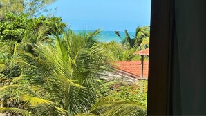 A view of a lush garden with palm trees and a red-roofed structure, likely a pool area, with a clear blue sky and ocean in the background. - Casa Da Costa (Aracati)