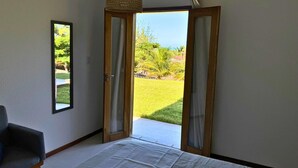 A bedroom with a large window, a bed, a chair, and a mirror on the wall. - Casa Da Costa (Aracati)