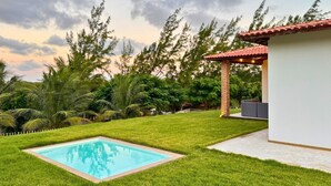 A backyard with a swimming pool, a patio area, and a small building with a red roof. - Casa Da Costa (Aracati)