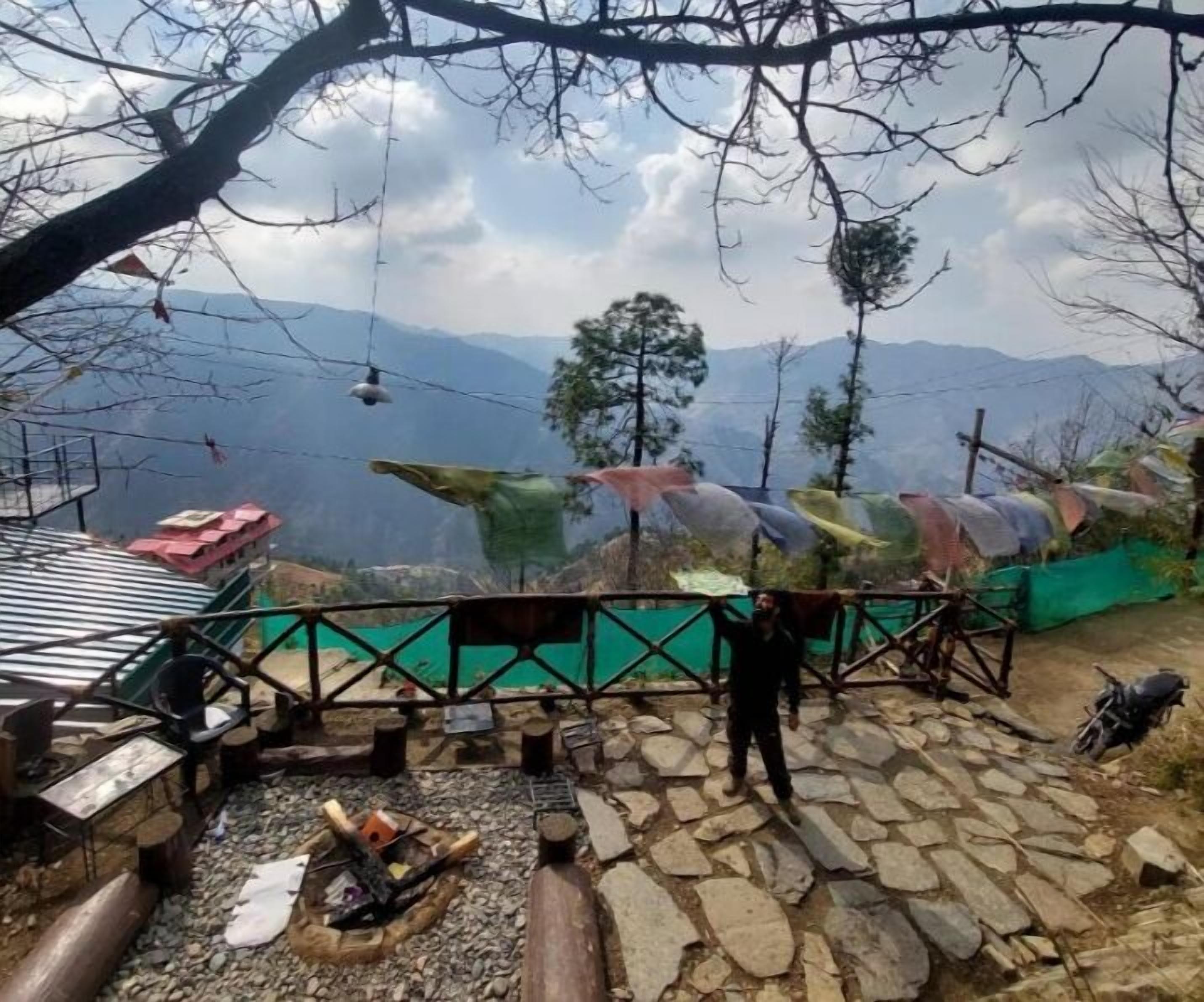 Un espacio empedrado con un brasero, una barandilla metálica y vistas a montañas al fondo.