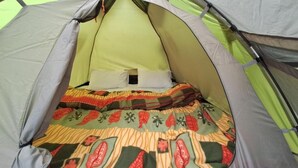A tent with a sleeping area inside, featuring a bed with a patterned blanket. - Delicate camp C (Kiar)