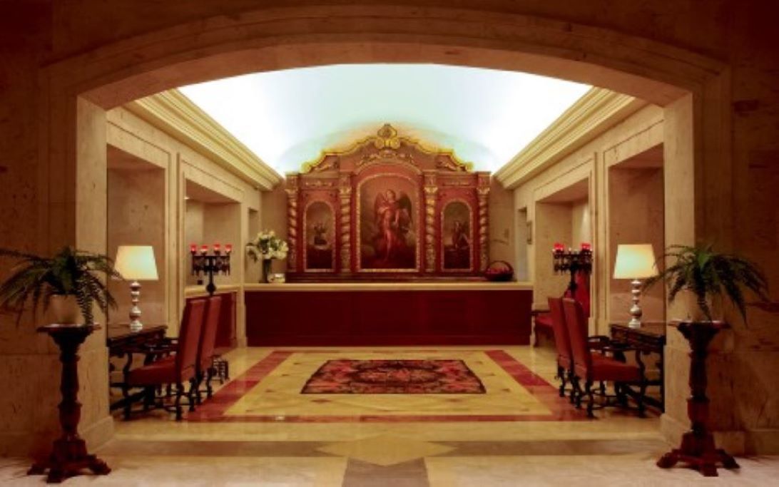 Un hall con mostrador de recepción, sillas rojas y un espejo grande y decorativo.