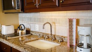 A kitchen with granite countertops, a stainless steel kettle, a coffee maker, and wooden cabinets.