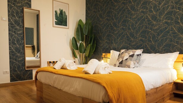 A neatly made bed with a yellow throw blanket, a large mirror, and a plant beside it. - Prime Living - [Apartment GOLD] on the Navigli (Milano)