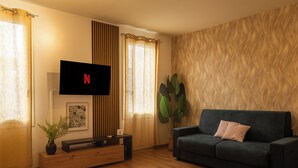 A living room with a flat-screen TV mounted on the wall, a dark sofa, a wooden coffee table, a potted plant, and a patterned wall. - Prime Living - [Apartment GOLD] on the Navigli (Milano)