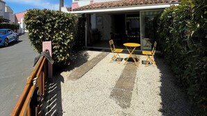 En bygning med en patio, hvor to gule stole og et bord står omgivet af grus og grønt.