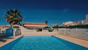 En swimmingpool med krystalklart, blåt vand, omgivet af en lav mur og en palme.