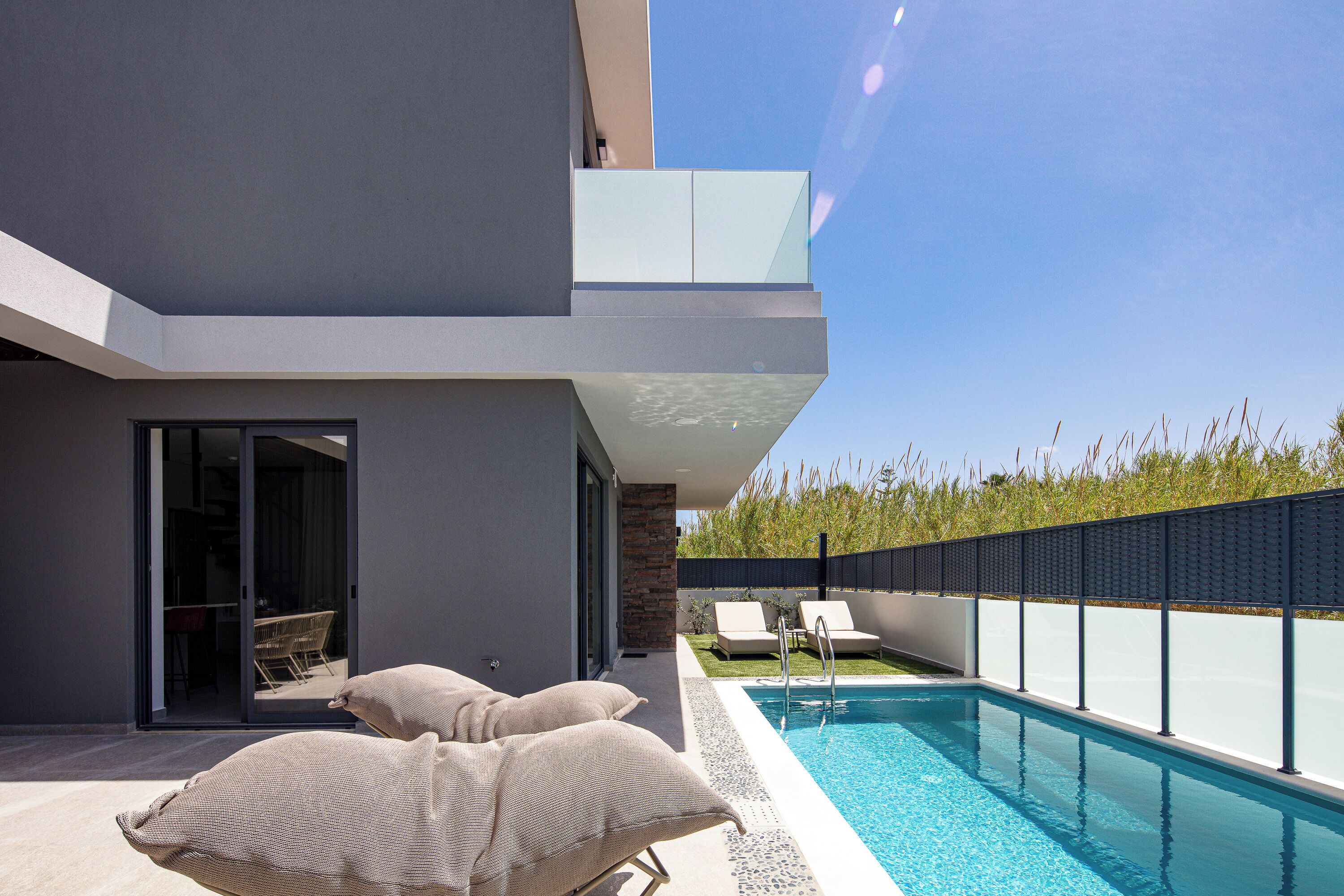 A modern outdoor pool area with a clear blue sky, a swimming pool, and two lounge chairs.
