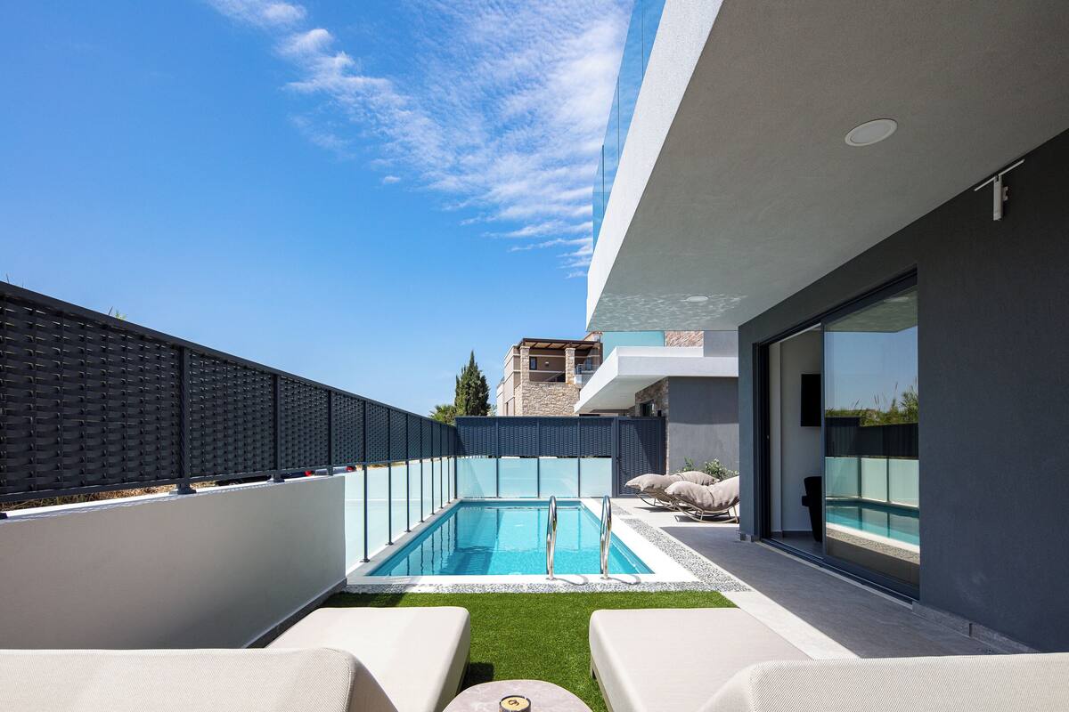 A rooftop pool with clear blue water, surrounded by a modern building with large windows and a view of the sky.