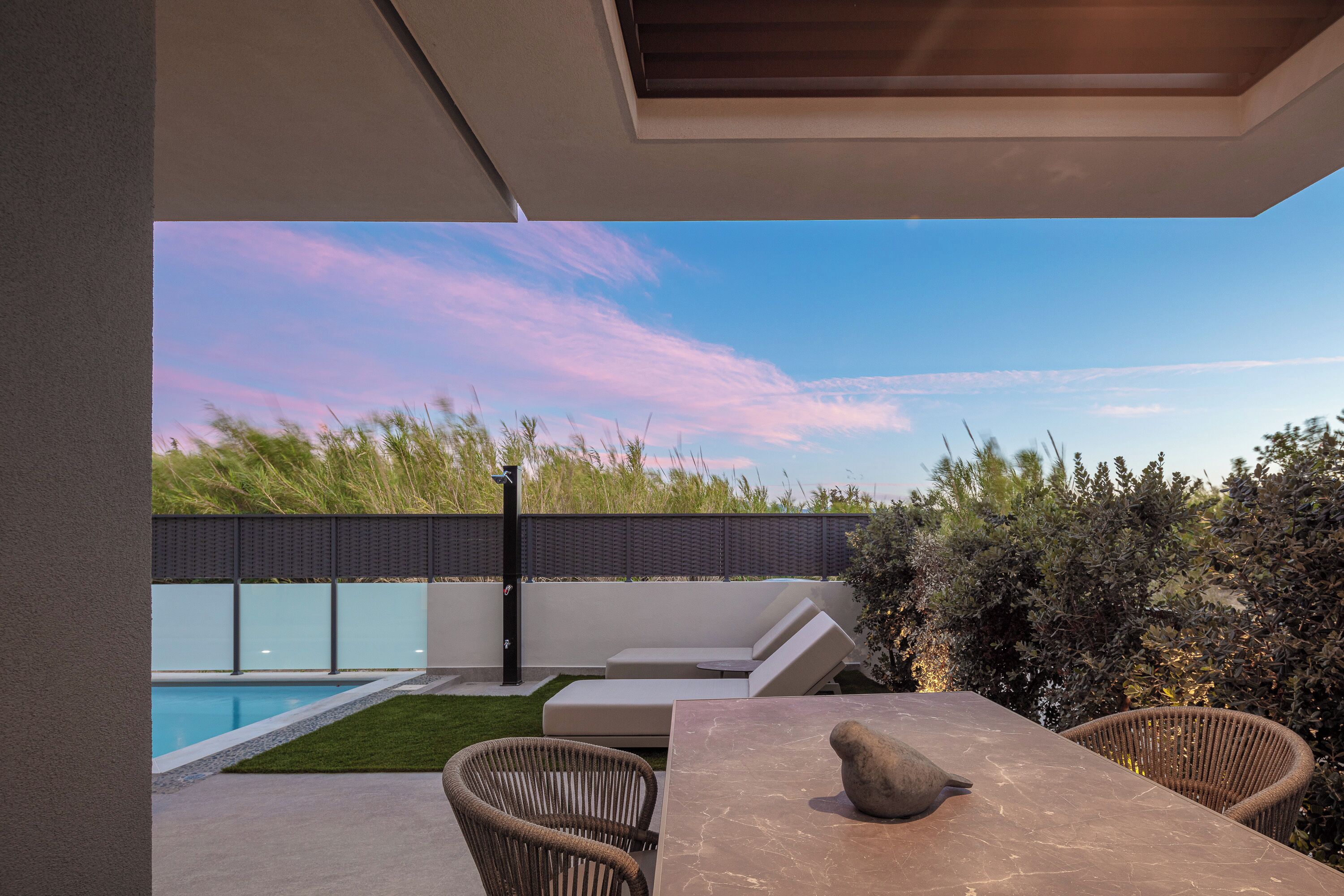 A modern outdoor patio with a pool, seating area, and a table with chairs.