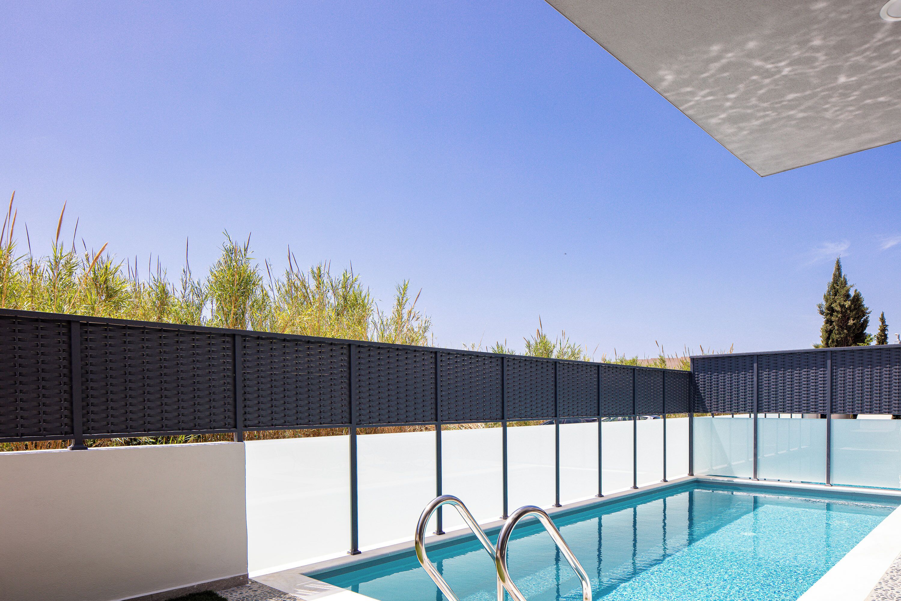 Una piscina con una escalera de metal, rodeada por un muro blanco y una valla negra.