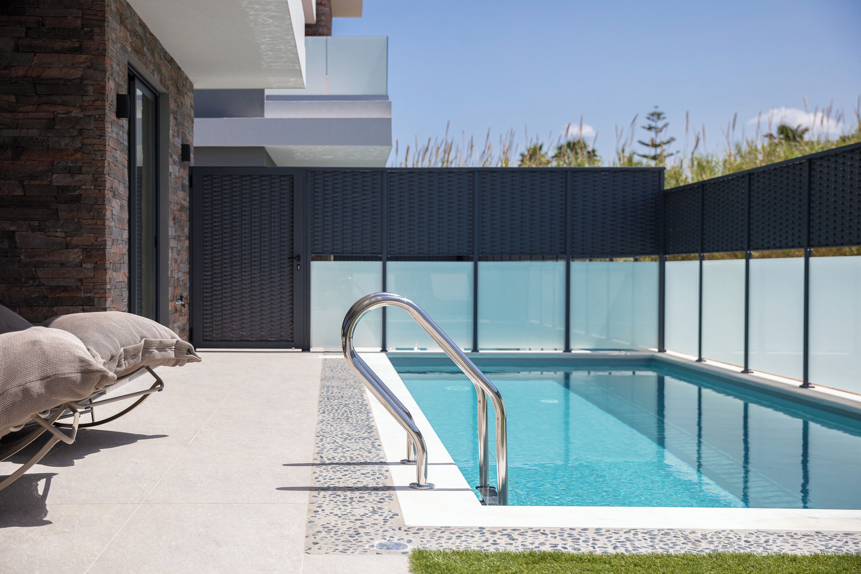 Zona de piscina exterior moderna amb una piscina d'un blau clar, una escala metàl·lica per a la piscina i un paviment de pedra.