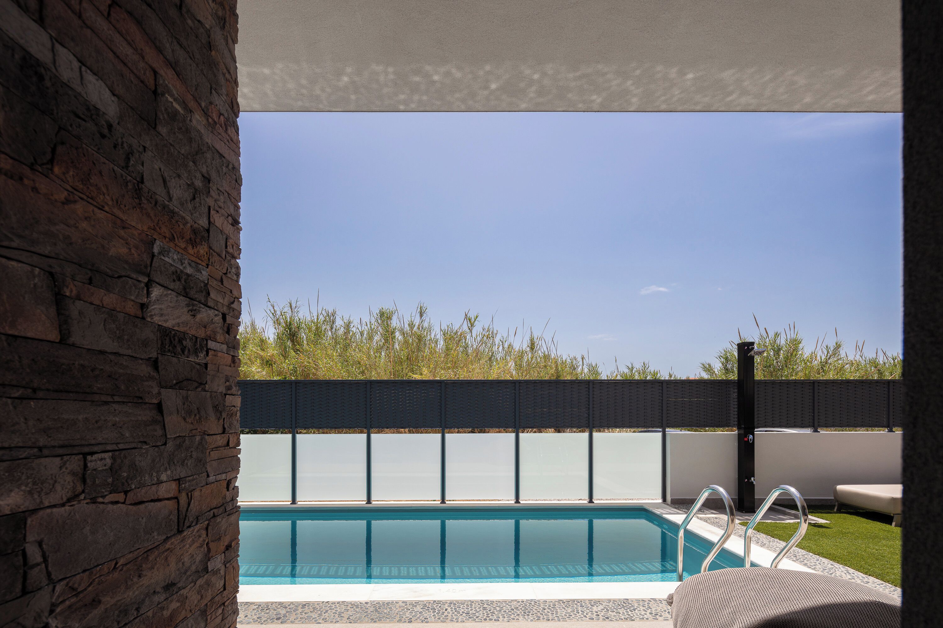 A swimming pool with a stone wall on one side and a view of a fence and greenery in the background.